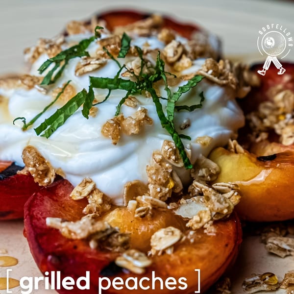 Grilled peaches topped with white cream, granola, and fresh mint, drizzled with honey.