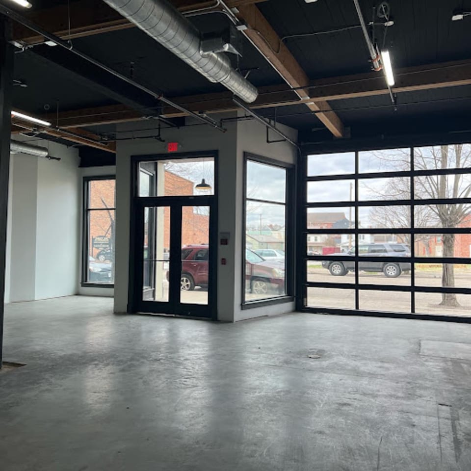 Empty Oddfellows restaurant interior with concrete floor, exposed ceiling, and large windows overlooking a street.