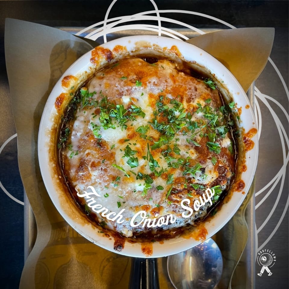 Oddfellows' French onion soup in a white bowl, topped with melted cheese and fresh parsley.