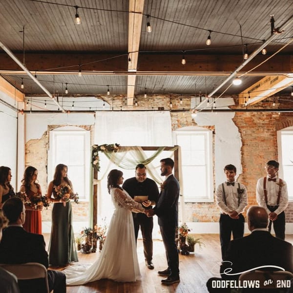 A wedding ceremony in a rustic Oddfellows venue with exposed brick, string lights, and wooden floors.