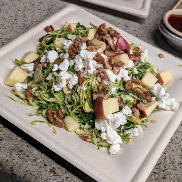 Oddfellows' salad with shredded greens, apples, pecans, and crumbled white cheese on a white plate.