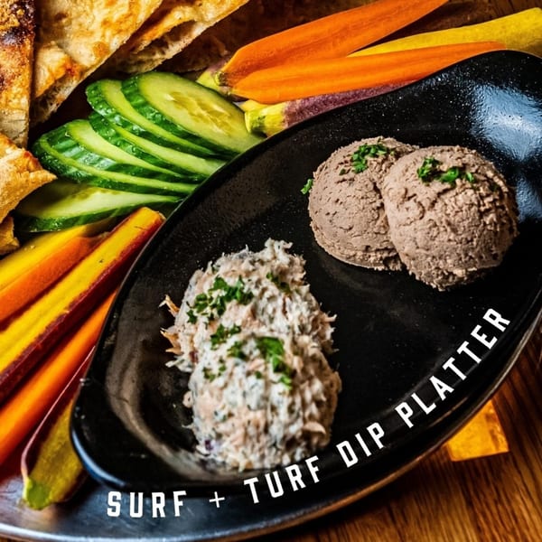 Oddfellows' Surf + Turf Dip Platter with two dips, sliced cucumbers, carrots, and flatbread.