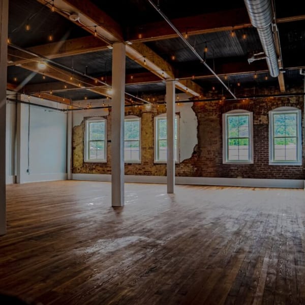 Empty Oddfellows restaurant interior with exposed brick, wooden floors, string lights, and large windows.