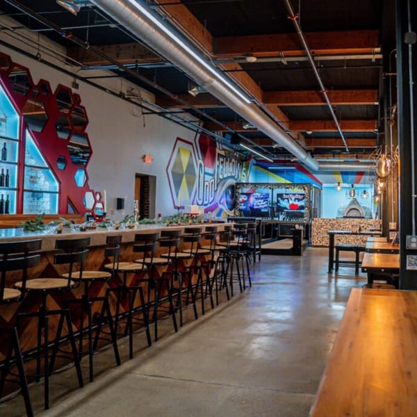 The interior of Oddfellows pizza restaurant, featuring a long bar with stools and a wood-fired oven.