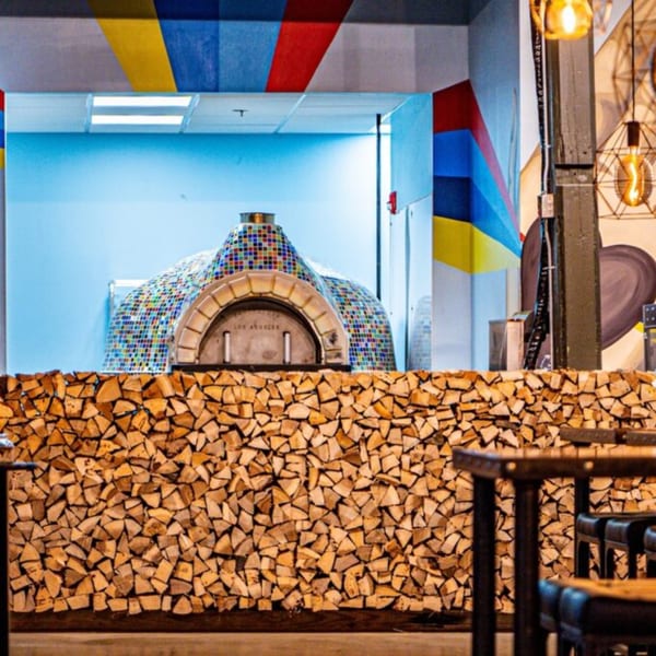 Oddfellows' pizza oven, tiled in colorful mosaic, sits behind a counter stacked with firewood.