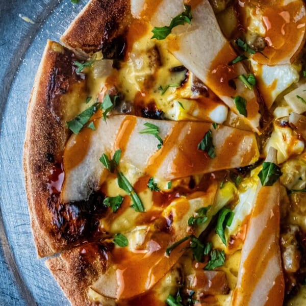 Close-up of an Oddfellows pizza with pears, cheese, and a balsamic glaze, garnished with herbs.