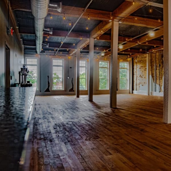 Oddfellows' spacious dining area with exposed brick, wooden beams, string lights, and large windows.