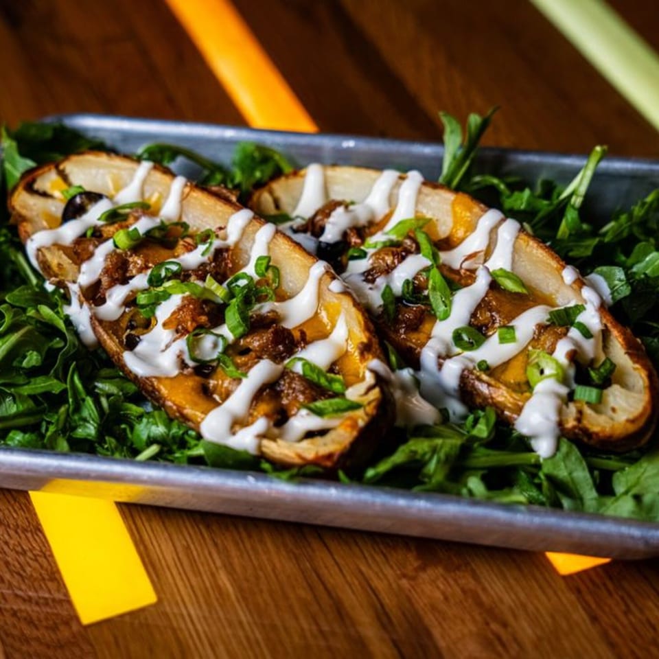 Two loaded potato skins with cheese, meat, sour cream, and green onions on a bed of greens.