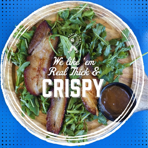 Crispy pork belly slices on a bed of arugula with a side of sauce, on a wooden plate.