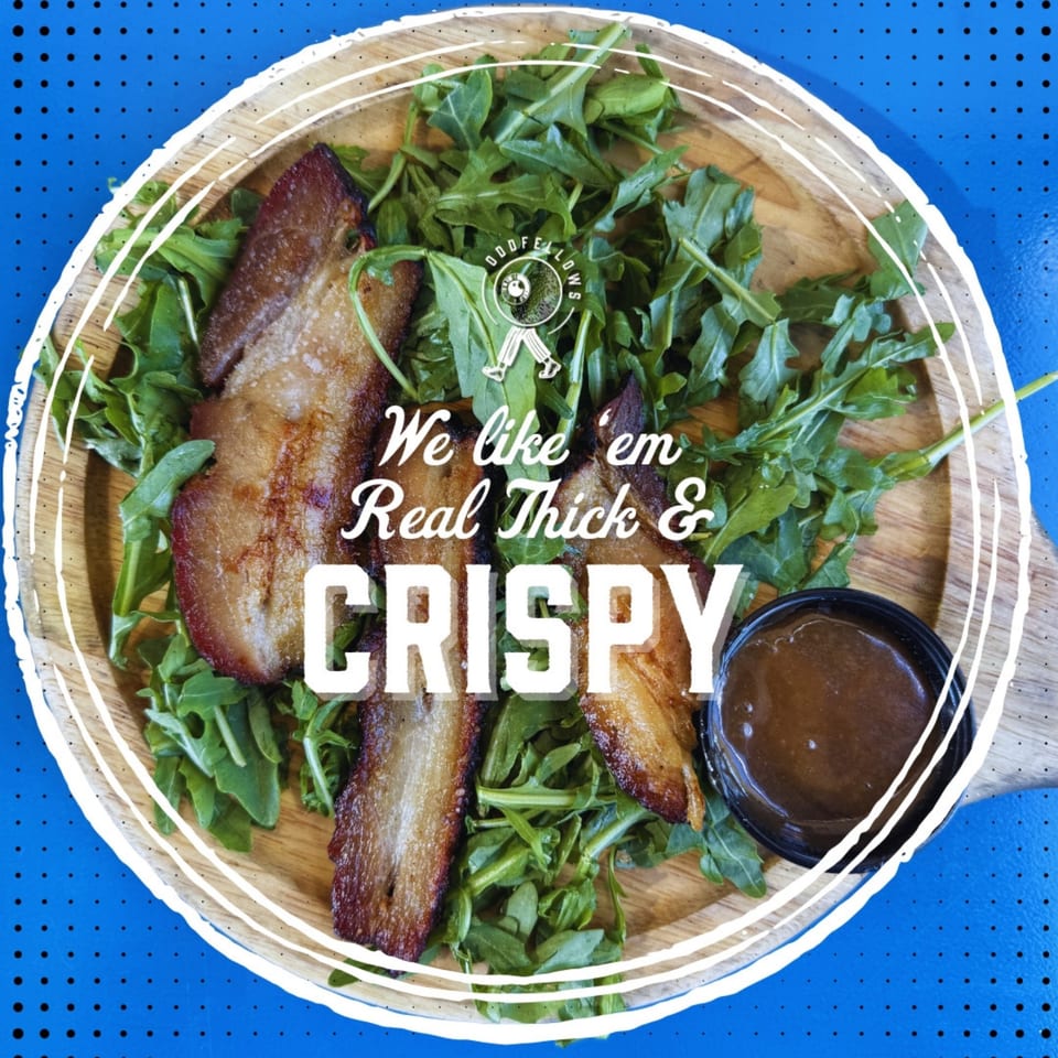 Crispy pork belly slices on a bed of arugula with a side of sauce, on a wooden plate.