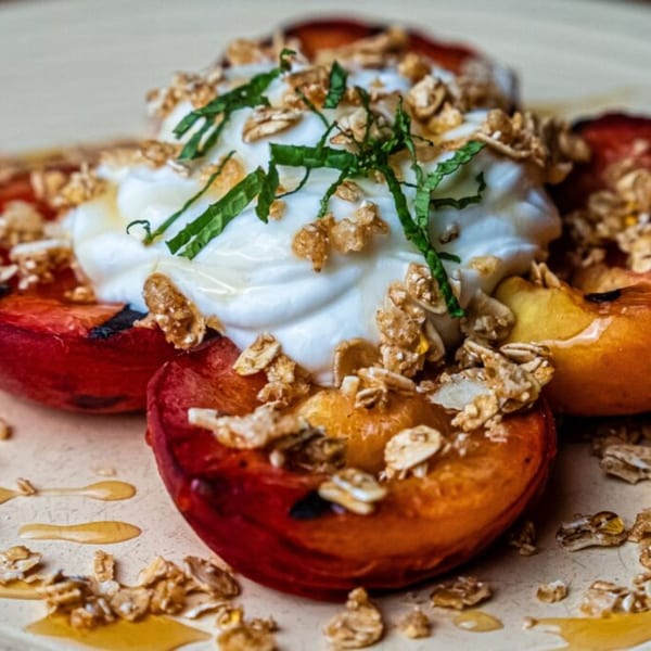 Grilled peaches topped with whipped cream, granola, mint, and a drizzle of honey.