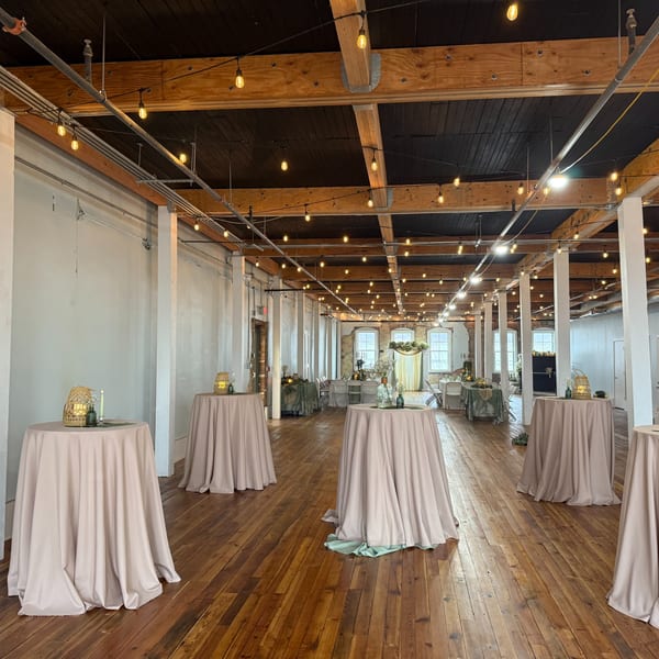 Oddfellows' event space with string lights, wooden floors, and round tables with light-colored tablecloths.