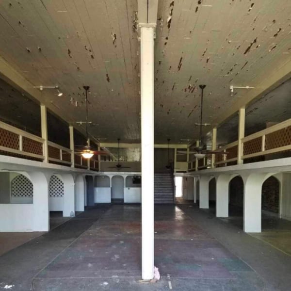 A large, empty, two-story room with a central white column, arched alcoves, and a peeling ceiling.