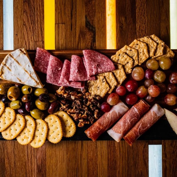 A charcuterie board with cheese, salami, prosciutto, olives, grapes, crackers, and nuts.