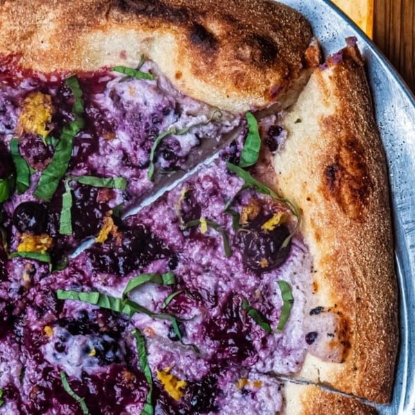 Close-up of a blueberry pizza with basil and lemon zest on a metal tray.