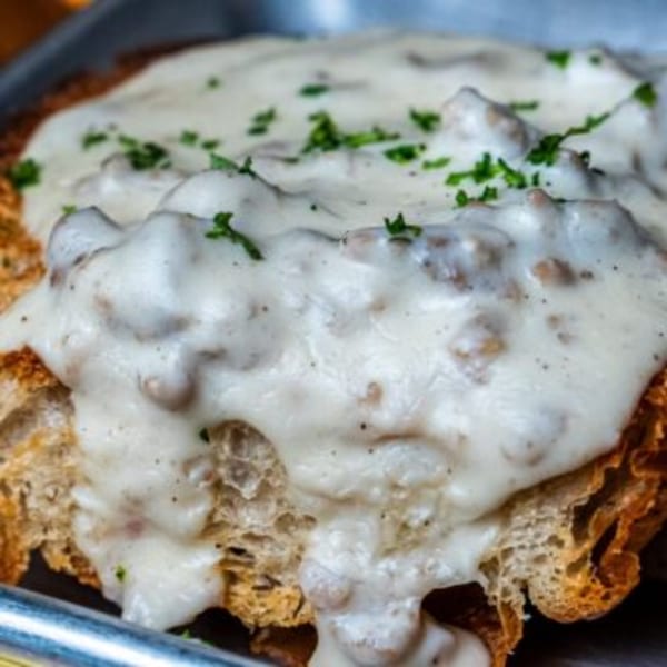 Close-up of biscuits and gravy, topped with fresh green herbs, on a metal tray.