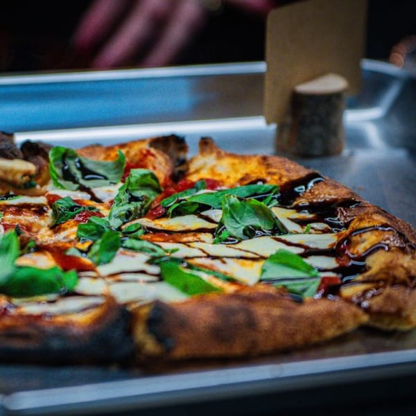 Oddfellows' pizza with fresh basil, mozzarella, and balsamic glaze on a metal tray.