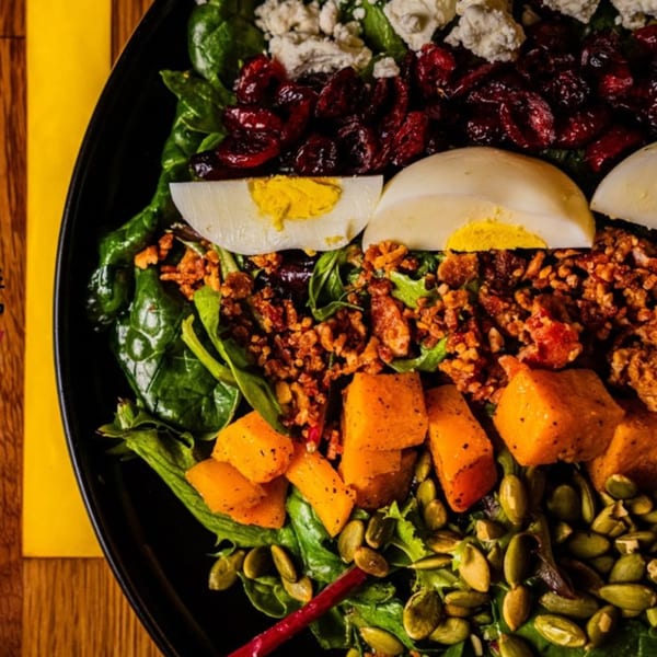 Close-up of a colorful Oddfellows salad with greens, dried cranberries, hard-boiled eggs, and pumpkin seeds.