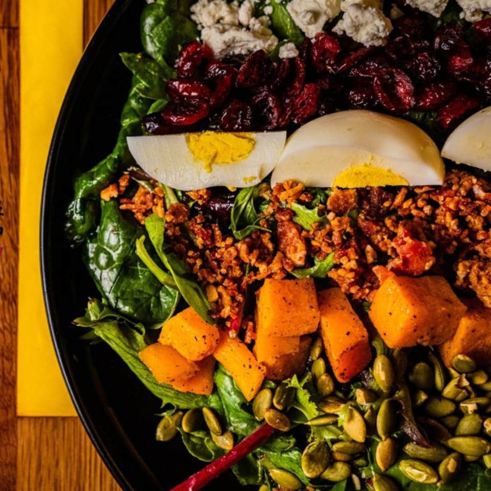Close-up of a colorful Oddfellows salad with greens, dried cranberries, hard-boiled eggs, and pumpkin seeds.